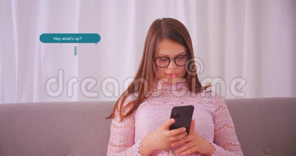 室内沙发上戴眼镜发短信的年轻美女特写照片视频的预览图