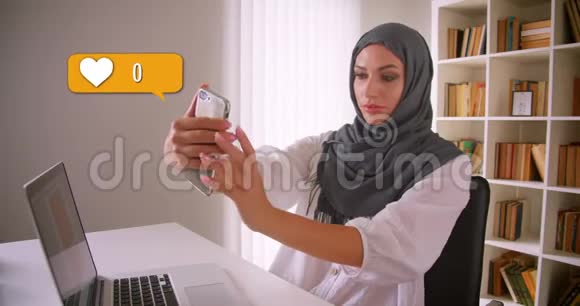 穆斯林女性戴头巾的特写照片在社交媒体上在办公室内使用手机获得点赞视频的预览图