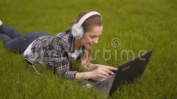 忙碌的商务女孩在笔记本电脑上工作女孩躺在公园的草地上打字4K视频的预览图