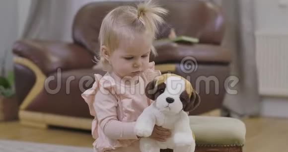 一个美丽的小女孩带着柔软的玩具狗走向镜头金发美女的特写镜头视频的预览图