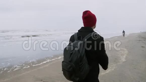 秋天戴着红帽子的杨人独自走过海滩视频的预览图