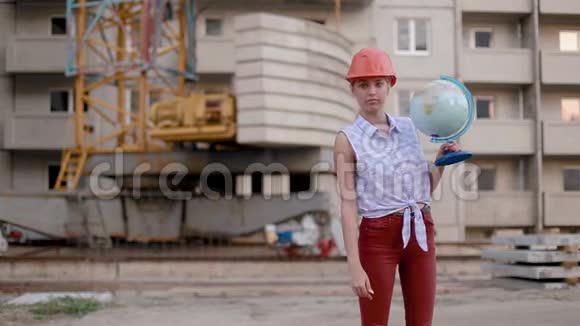 戴着建筑头盔的漂亮年轻女子手里拿着地球仪把它扭来扭去表现出良好姿态视频的预览图