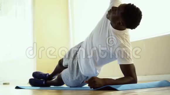 非裔美国运动员在健身房垫子上做侧板运动时单臂平衡视频的预览图