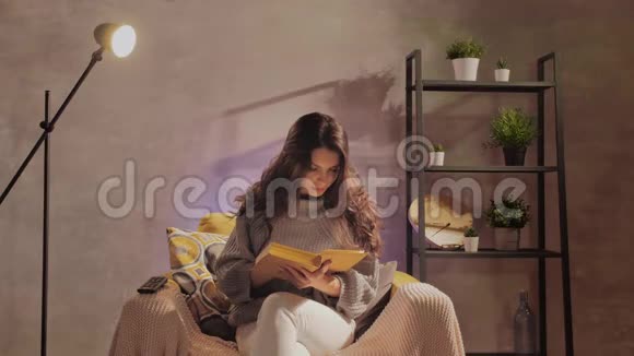 一个年轻的女人坐在椅子上看书女孩在温暖的房间里的舒适沙发上做梦视频的预览图