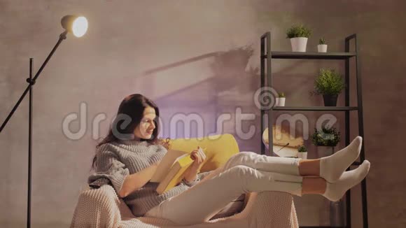 一个年轻的女人坐在椅子上看书女孩在温暖的房间里的舒适沙发上做梦视频的预览图