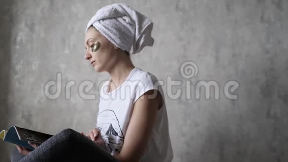 在家里放松一个年轻的女人在毛巾和眼罩阅读杂志健康提升美容护理视频的预览图