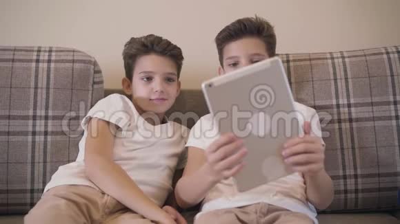 前景特写两个高加索双胞胎兄弟看着平板电脑屏幕微笑小兄弟靠在视频的预览图
