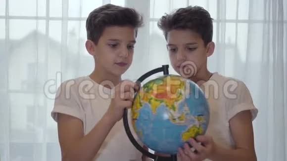 黑种人白人小学生拿着地球仪向他的孪生兄弟解释地理的特写照片兄弟姐妹视频的预览图