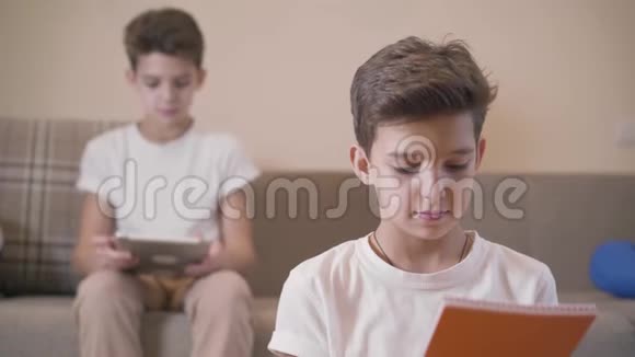 小男孩看书时的特写肖像回头看着他的双胞胎弟弟他拿着平板电脑坐在视频的预览图
