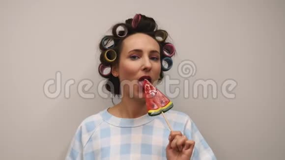 女性测试糖果棒棒糖靠白墙年轻快乐的女人有着卷发和明亮闪亮的妆容舔着五颜六色的糖果视频的预览图
