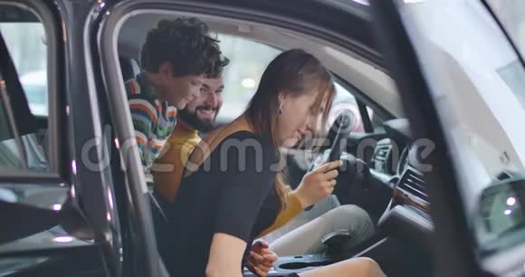 侧面观看快乐的白种人妻子坐在汽车沙龙与家人和讨论购买年轻的女商人视频的预览图