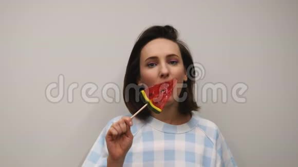 女舔棒棒糖在工作室年轻的微笑女孩嘴唇享受糖果女人在白色背景下舔糖果视频的预览图
