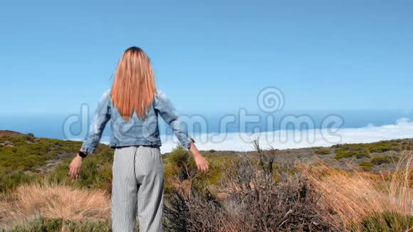 年轻女子伸出双臂站在山顶上观看美丽的风景视频的预览图