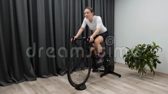 骑着智能教练在室内骑自行车准备在静止自行车上进行硬踏板有氧运动自行车的概念视频的预览图