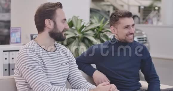 侧面看两个白人英俊的男人坐在汽车经销商微笑和交谈年轻的商人讨论视频的预览图
