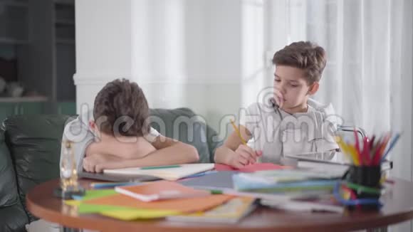 可爱的白种人男孩醒来他的孪生兄弟坐在桌子旁小兄弟在家一起做作业视频的预览图