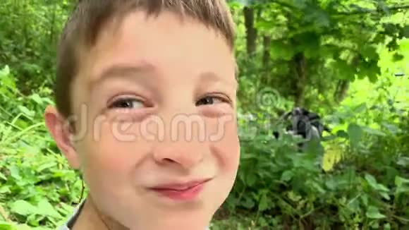 一个十几岁的男孩的肖像他在镜头前微笑他坐在夏天的森林里绿色的树叶上视频的预览图