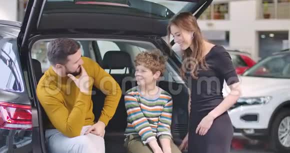 汽车经销商中快乐白人家庭的肖像成功的商人和儿子坐在大敞篷车厢里视频的预览图