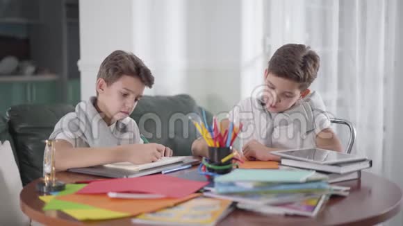 两个富有创造力的高加索双胞胎兄弟坐在桌子旁用五颜六色的铅笔画画可爱的男孩看着他的兄弟视频的预览图