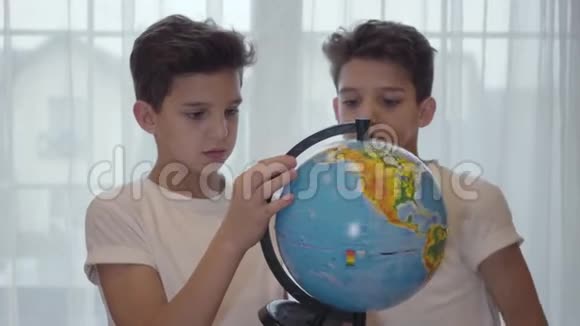 两个高加索双胞胎兄弟看着地球仪说话小兄弟在家一起学习教育地理视频的预览图