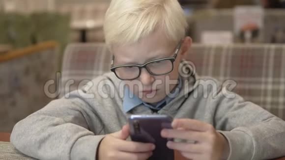 一个戴眼镜的严肃男孩坐在咖啡馆里玩手机视频的预览图