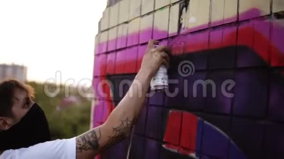 涂鸦艺术家画与气溶胶男人穿着巴拉克拉瓦和白色T恤带喷雾瓶年轻的城市画家视频的预览图
