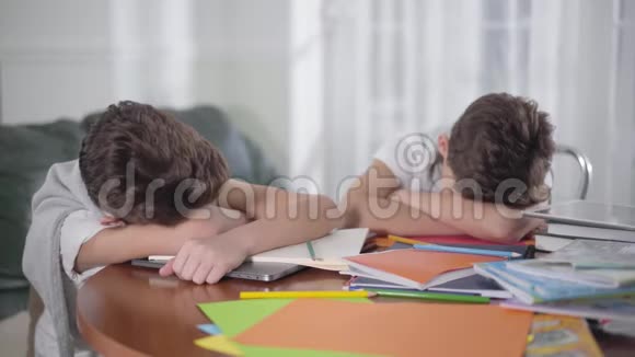 年轻的白种人黑发男孩醒来伸展他的兄弟或朋友睡在桌子上小兄弟倒下了视频的预览图