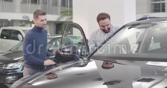 男性白种人汽车经销商打开车门成年男子坐进沙龙年轻人在讨论买卖交易视频的预览图