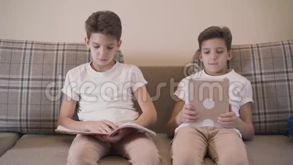 年轻的高加索小学生坐在沙发上拿着笔记本的画像他的孪生兄弟给他看了一些东西视频的预览图