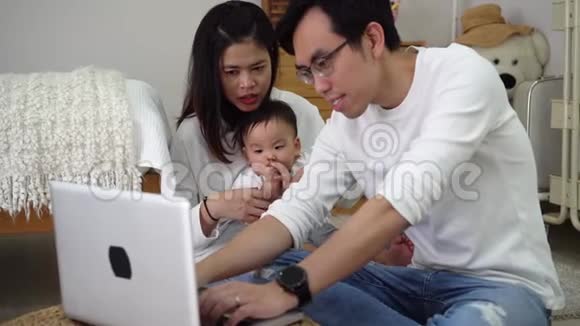 亚洲父亲和妻子一起用笔记本电脑工作还有一个可爱的亚洲小男孩坐在家里舒适的房间里视频的预览图