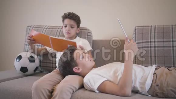 两个白人学生在家里沙发上休息双胞胎兄弟穿着类似的衣服在室内看书一个男孩视频的预览图