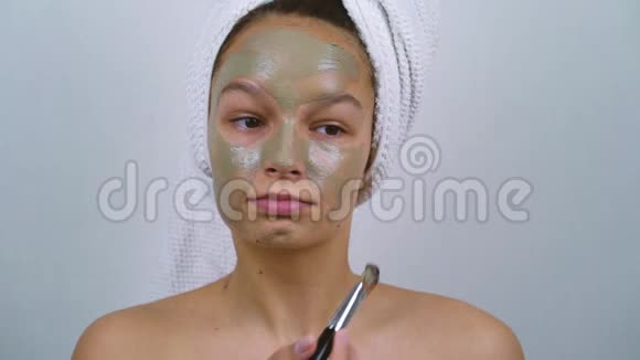 青少年穿着浴巾在家庭水疗中心的脸上涂粘土面具视频的预览图