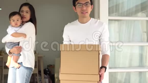 开朗的亚洲父母抱着可爱的婴儿和盒子带着物品在搬进新房子时看着相机青年视频的预览图