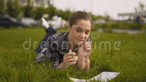 热情的学生女孩在笔记本上做笔记公园绿草如茵4K视频的预览图