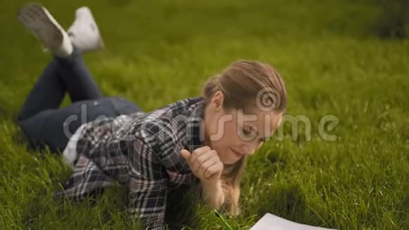 女孩躺在草地上在笔记本上做笔记公园绿草如茵4K视频的预览图