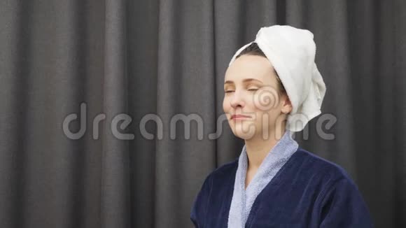 年轻女性从头上摘下毛巾洗澡后抚摸她湿漉漉的头发洗澡后穿蓝色浴袍的女士视频的预览图