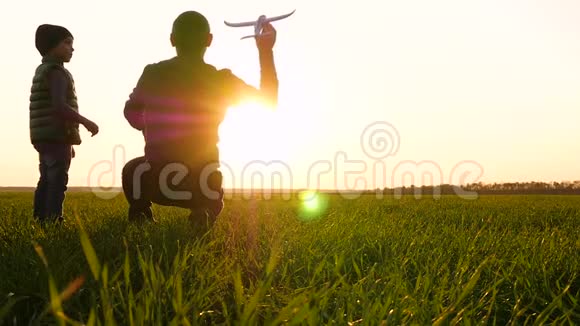 一位快乐的父亲和他的儿子在夕阳下的绿色草地上玩耍一个男人和一个孩子把玩具飞机发射到视频的预览图