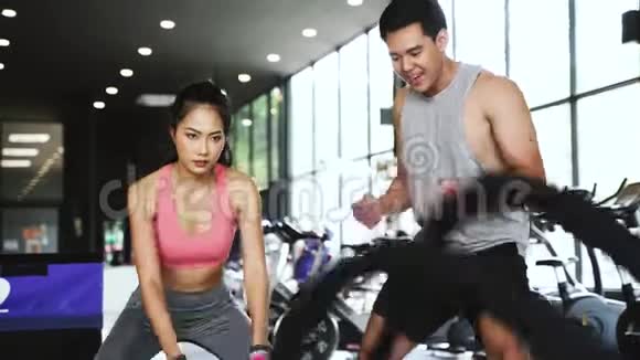 亚洲私人教练指导一名健美女子在健身馆进行交叉式绳索练习视频的预览图