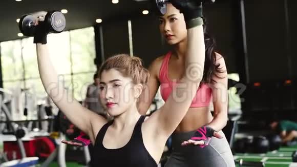亚洲私人教练指导一位健美女士在健身中与哑铃一起进行举重练习视频的预览图