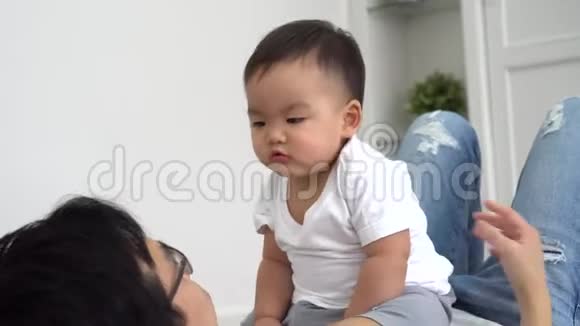 可爱的亚洲小男孩坐在父母身上在周末休息时抚摸父亲的脸视频的预览图