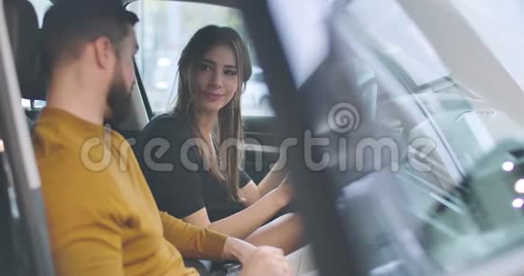 侧面的观点年轻的高加索女孩看着她的丈夫就像坐在汽车沙龙丈夫和妻子选择视频的预览图