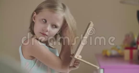 金发白种人小女孩看手镜和修头发的肖像穿着粉红色蓝色裙子的可爱孩子视频的预览图