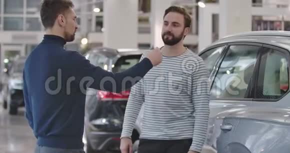 后侧观看白种人汽车经销商的休闲服装给汽车钥匙给客户和握手快乐男视频的预览图