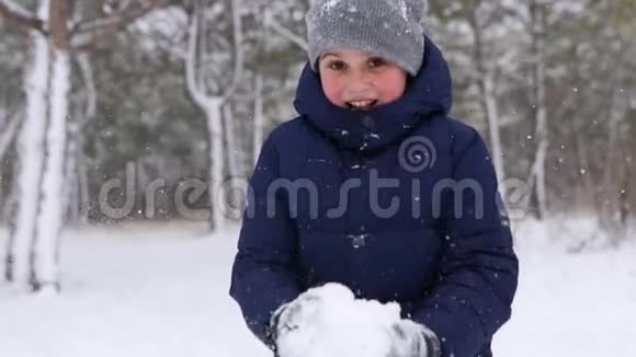 穿着海军夹克的快乐男孩玩雪在寒冷的冬天把它扔到森林里的空气中性格开朗的孩子视频的预览图