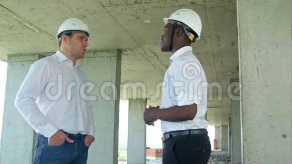 英俊的建筑商人戴着防护头盔和背心在建筑工地握手视频的预览图