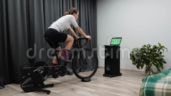 骑自行车的女人在聪明的教练适合白种人女子自行车训练看电脑屏幕赛车在线视频的预览图