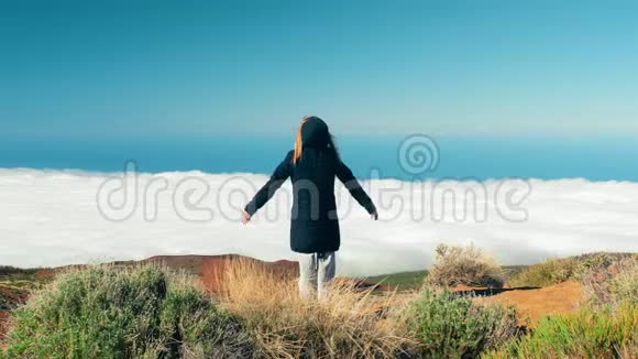 快乐的女人独自站在云层之上的山峰上在美丽的风景早晨举起手臂视频的预览图