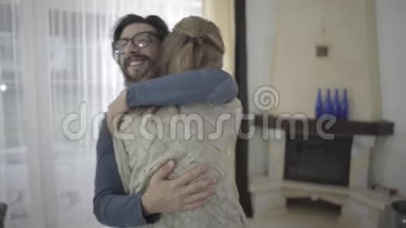 快乐的白人夫妇在家拥抱和旋转戴眼镜的满脸胡须的男人拥抱他可爱的妻子或视频的预览图