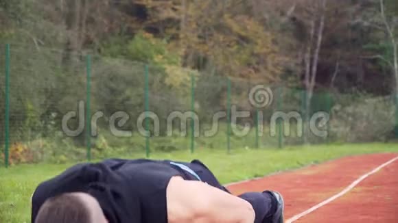 4k倾斜运动视频年轻的健身男子做俯卧撑在户外跑步跑道视频的预览图