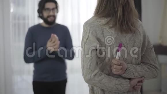 年轻的白种人女人背着两条条纹进行妊娠试验笑容满面的丈夫视频的预览图